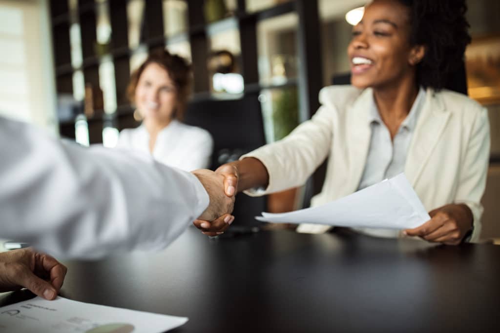 A woman on an interview shaking a hand with an interviewer | TGC Search Staffing | Executive Recruiters