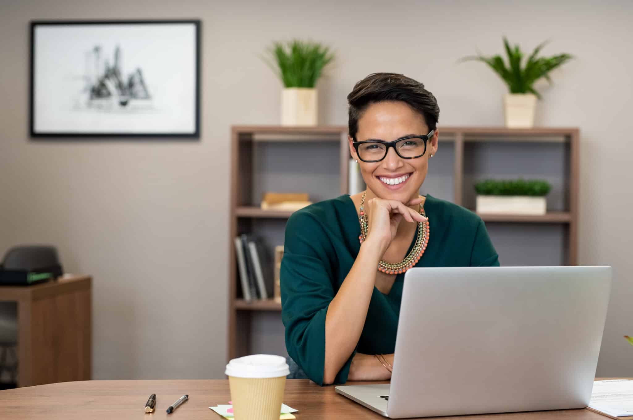 Lady with short hair cut smiling, sitting behind her laptop with a cup of coffee in the office | Executive Assistant | How to become an executive assistant