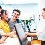Receptionist dressed in a white shirt assist a group of laughing people
