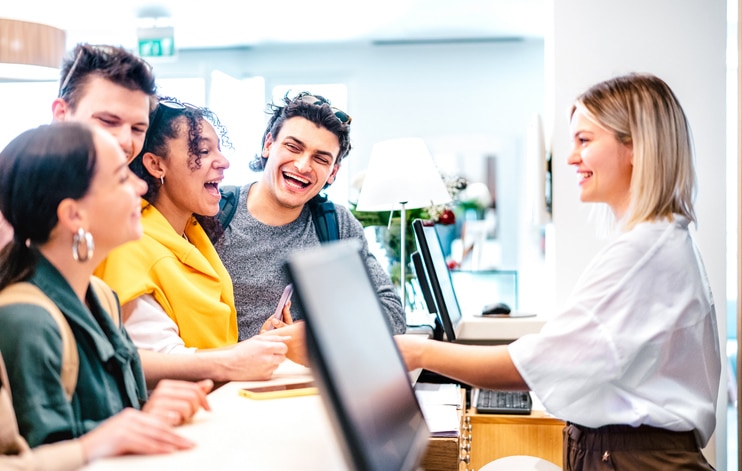 Receptionist dressed in a white shirt assist a group of laughing people